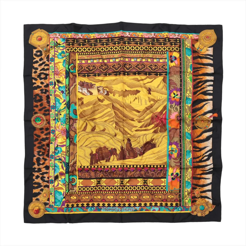 Hermès Carré 90 La Femme aux Semelles de Vent silk scarf with black border, golden landscape, floral panels, leopard and tiger-print details.