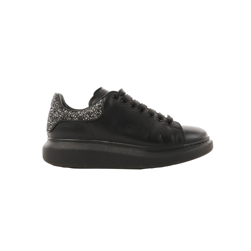 Side view of black leather Alexander McQueen platform trainer with black laces and a glitter heel tab on a white background.