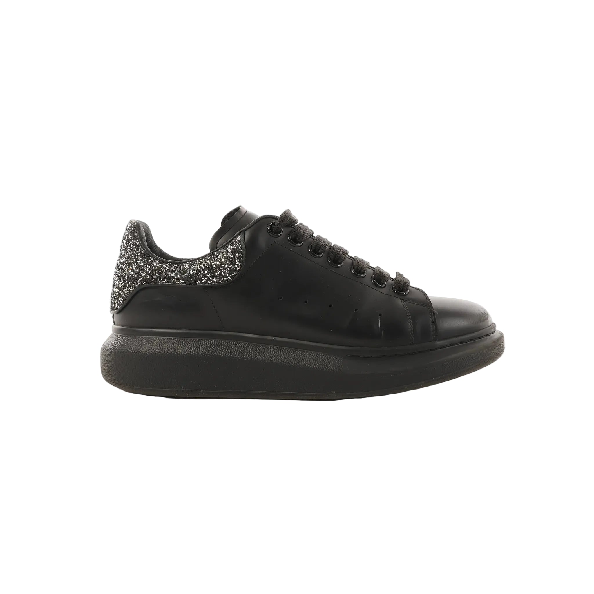 Side view of black leather Alexander McQueen platform trainer with black laces and a glitter heel tab on a white background.