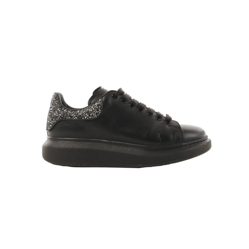 Side view of black leather Alexander McQueen platform trainer with black laces and a glitter heel tab on a white background.
