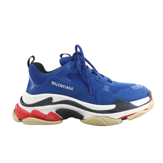 Balenciaga Triple S sneakers in blue faux leather with mesh panels, white Balenciaga logo on the side, chunky multicolor sole in beige, black, white, and red, shown in side view on a white background.