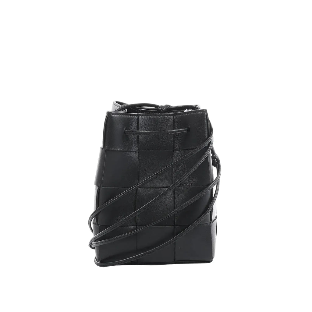 Bottega Veneta Cassette mini bucket bag in black maxi intrecciato woven leather with drawstring top and thin crossbody strap on a white background.