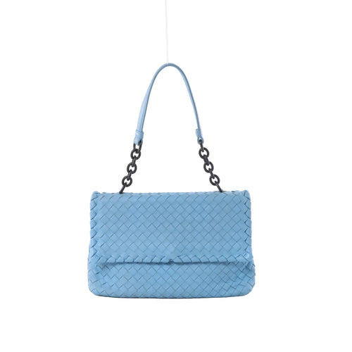 Light blue Bottega Veneta Intrecciato woven leather shoulder bag with a flap front, dark chain links and matching blue leather strap on a grey background.