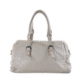 Light gray Bottega Veneta Boston handbag in Intrecciato woven leather with dual top handles, buckle details and dark metal hardware on a white background.