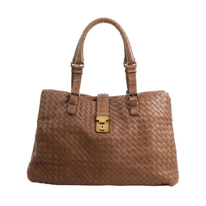 Front view of a Bottega Veneta Intrecciato Roma handbag in brown woven leather, featuring double rolled handles, adjustable buckles, and a central flap with gold-tone lock closure.