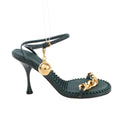 Bottega Veneta green leather heel sandal featuring a sculpted stiletto heel, ankle strap with gold buckle and hanging orb charm, gold chain front strap, and textured footbed, displayed on a white background.