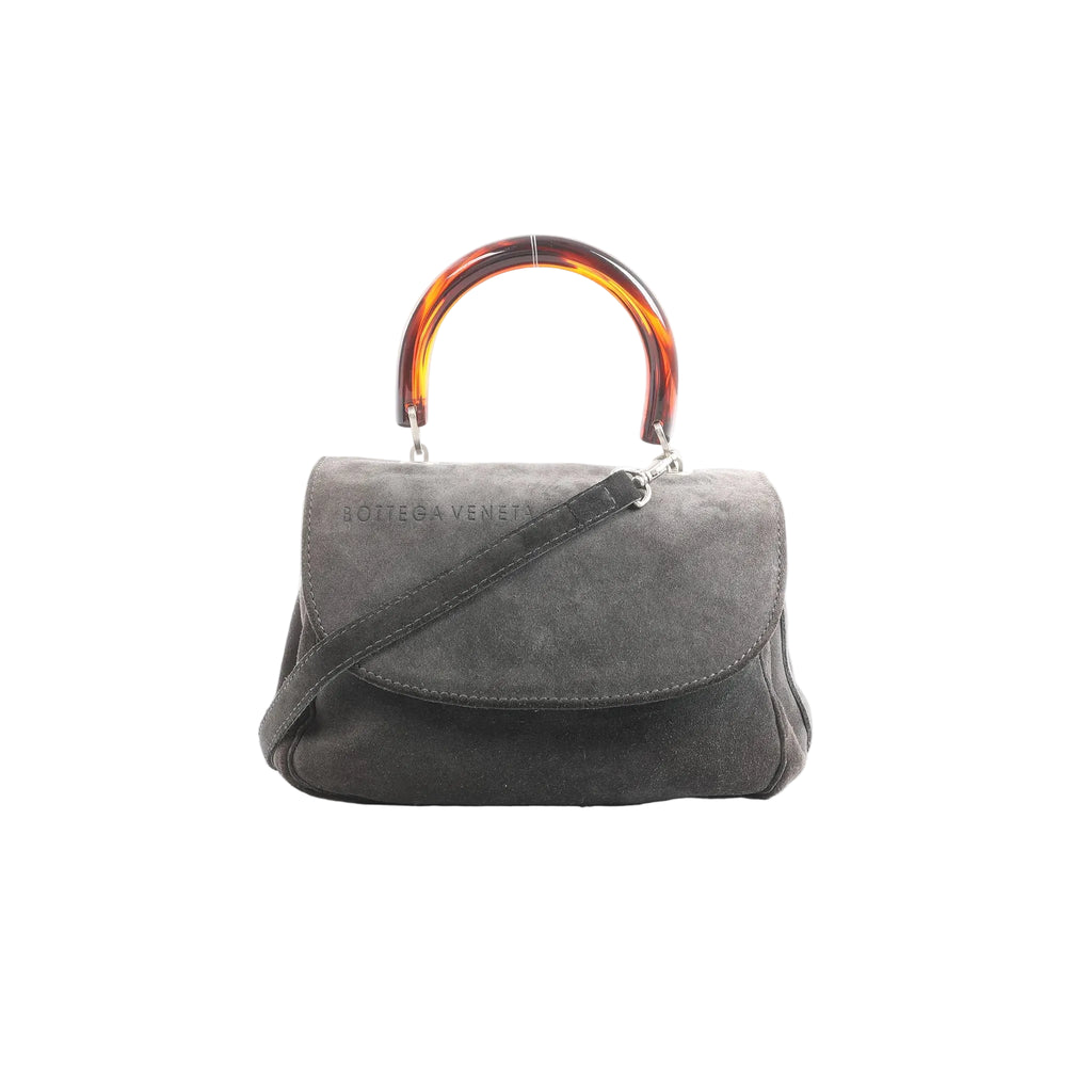 Bottega Veneta gray suede handbag with tortoiseshell-effect top handle, flap front, and detachable shoulder strap, front view on white background.