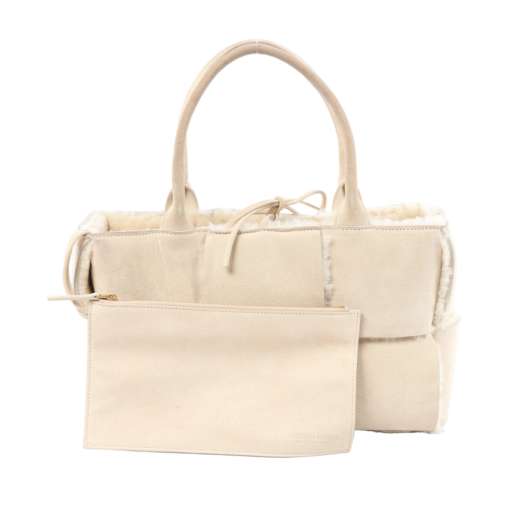 Bottega Veneta Arco Maxi Intrecciato beige leather and shearling handbag with top handles and matching zip pouch on white background.