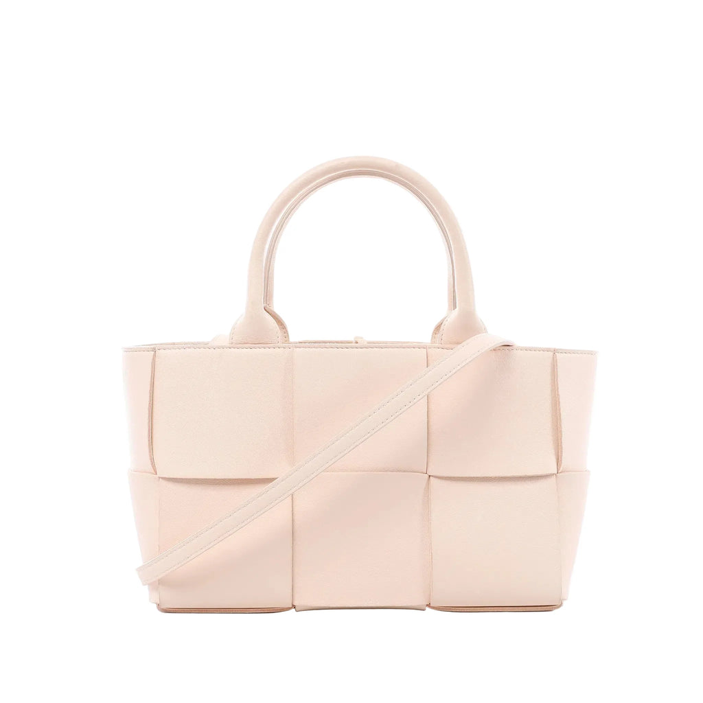 Bottega Veneta Arco handbag in pale pink Maxi Intrecciato woven leather with rounded top handles and slim shoulder strap on white background.