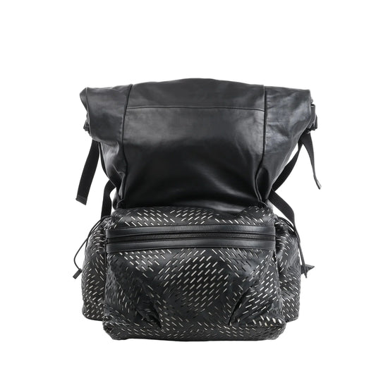 Bottega Veneta black leather backpack with perforated pattern on the front and side pockets, large flap closure, top zipper compartment, and adjustable shoulder straps against a white background.
