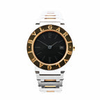 Close-up of a Bvlgari BB26SGD watch featuring a black dial, date display at 3 o’clock, yellow gold bezel engraved with “BVLGARI,” and a two-tone stainless steel and gold bracelet.