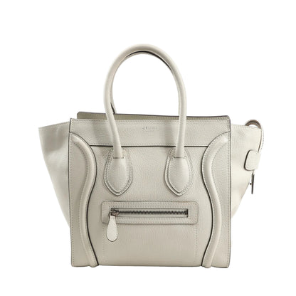 Celine Luggage Micro Handbag in ecru grained leather, featuring a structured design with top handles, front zip pocket, curved stitched detailing, and side gussets, displayed against a white background.