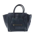 Front view of a navy blue Celine Luggage Micro leather handbag with winged sides, rolled top handles and a gold-tone front zip pocket.