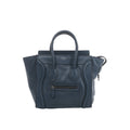 Front view of Celine Luggage Micro navy blue grained leather handbag with flared sides, rounded handles, curved leather trim and a front zip pocket.