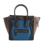 Celine Luggage Micro handbag in blue leather with black trim, taupe side panels, top handles, and front zip pocket on white background
