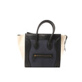 Celine Luggage Mini handbag in navy leather with black trim and ivory side panels, top handles, and front zip pocket, shown on a white background.