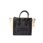 Celine Luggage Mini handbag in navy leather with black trim and ivory side panels, top handles, and front zip pocket, shown on a white background.