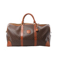 Front view of Celine Macadam brown monogram PVC Boston travel bag with tan leather trim, dual top handles, zip-top closure, hanging leather tag, and padlock on a white background.