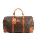 Celine Macadam Boston travel bag in brown PVC with tan leather trim, dual handles, gold-tone hardware, and structured silhouette.