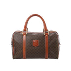 Front view of Celine Macadam Boston brown monogram PVC handbag with tan leather top handles, leather trim, zip-top closure, and front logo patch on a white background.