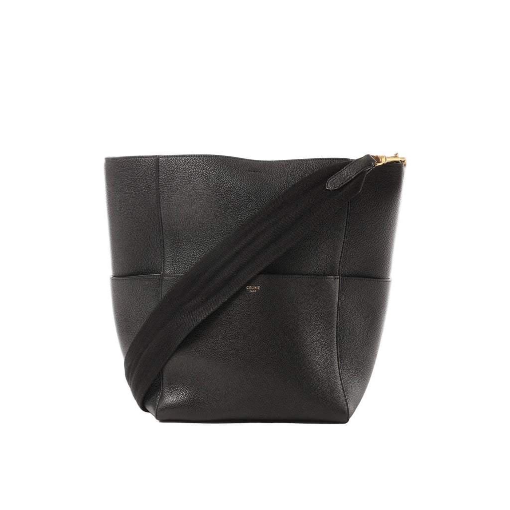 Black Celine Seau Sangle leather bucket shoulder bag with wide black web strap and small gold Celine Paris logo, shown on a white background.