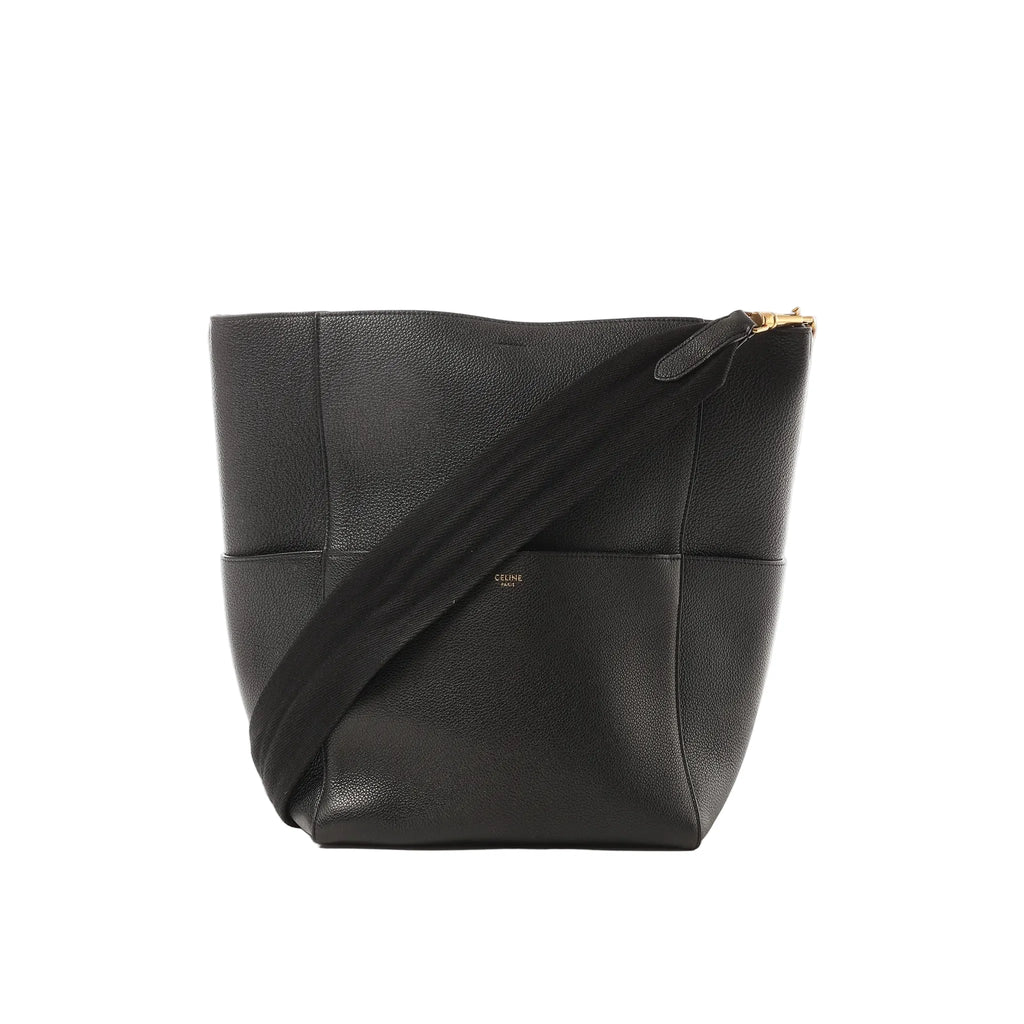 Black Celine Seau Sangle leather bucket shoulder bag with wide black web strap and small gold Celine Paris logo, shown on a white background.