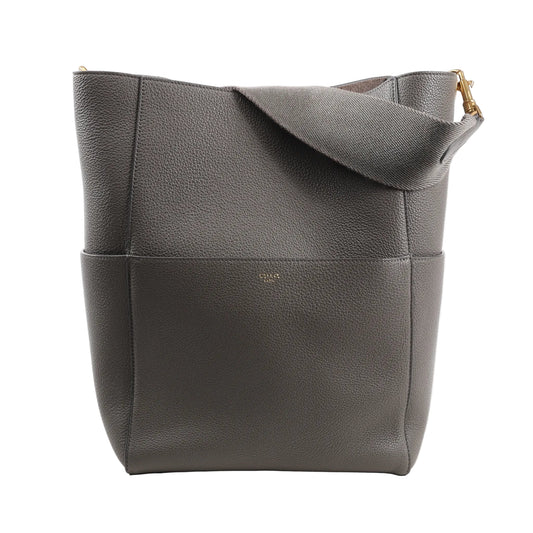 CELINE Seau Sangle Bucket Shoulder Bag in gray grained leather with a wide strap, gold-tone hardware, and subtle logo embossing, standing upright against a white background.