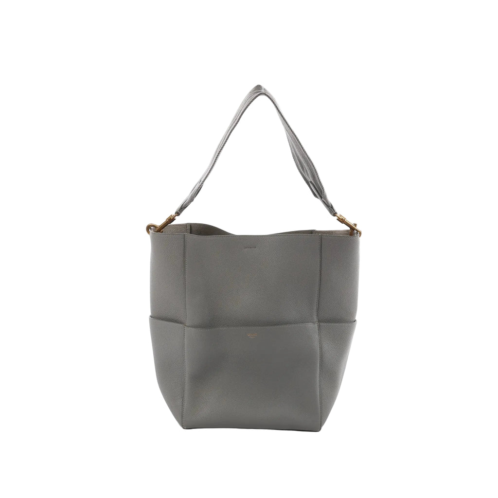 CELINE Seau Sangle bucket shoulder bag in gray pebbled leather with wide fabric shoulder strap and gold-tone hardware on a white background.