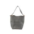 CELINE Seau Sangle bucket shoulder bag in gray pebbled leather with wide fabric shoulder strap and gold-tone hardware on a white background.