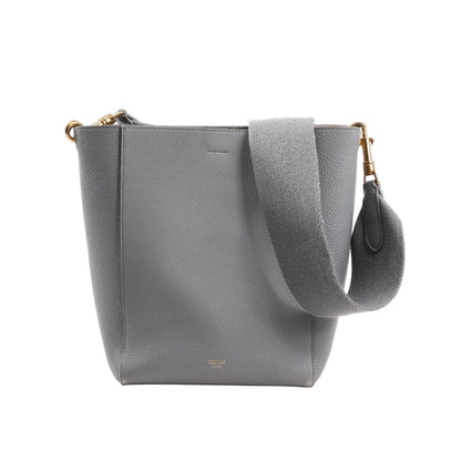 CELINE Seau Sangle Bucket Mini Shoulder Bag in gray grained leather with a wide adjustable strap, gold-tone hardware, and minimalist logo stamp at the bottom front, displayed upright on a white background.