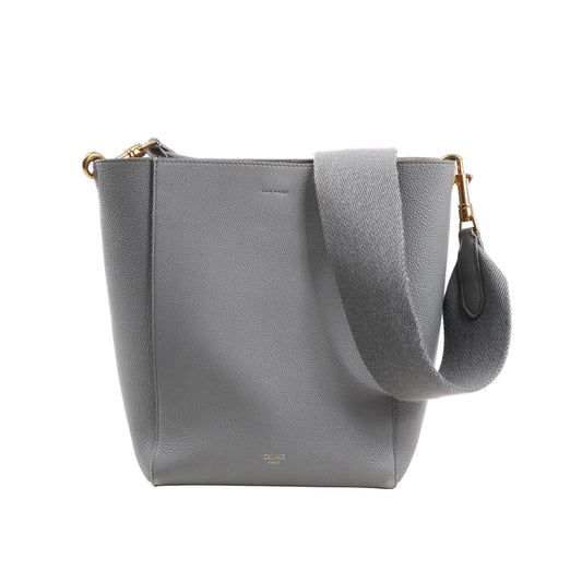 CELINE Seau Sangle Bucket Mini Shoulder Bag in gray grained leather with a wide adjustable strap, gold-tone hardware, and minimalist logo stamp at the bottom front, displayed upright on a white background.