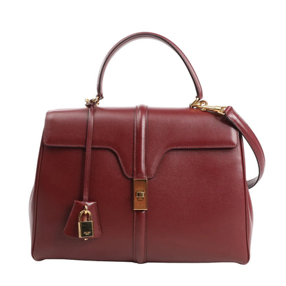 Celine Sac 16 Medium handbag in smooth burgundy leather with a structured silhouette, top handle, detachable shoulder strap, gold-tone turn-lock closure, and matching padlock charm.