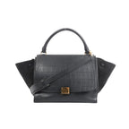 Black Celine Trapeze handbag in croc-embossed leather and suede with top handle, shoulder strap, side wing panels, and gold-tone front clasp on a white background
