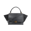 Black Celine Trapeze handbag in croc-embossed leather and suede with top handle, shoulder strap, side wing panels, and gold-tone front clasp on a white background