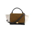 Celine Trapeze handbag with brown suede front flap, white leather side panels, black leather base and handle, gold clasp, and black strap on white background