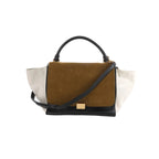 Celine Trapeze handbag with brown suede front flap, white leather side panels, black leather base and handle, gold clasp, and black strap on white background
