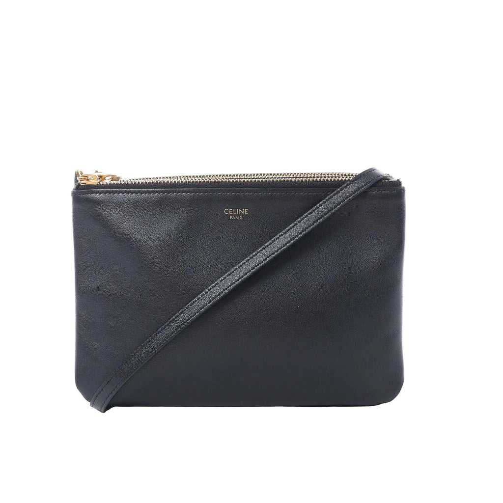 Celine Trio Small black leather crossbody bag with slim shoulder strap, gold-tone zip closure, and small Celine Paris logo on white background.