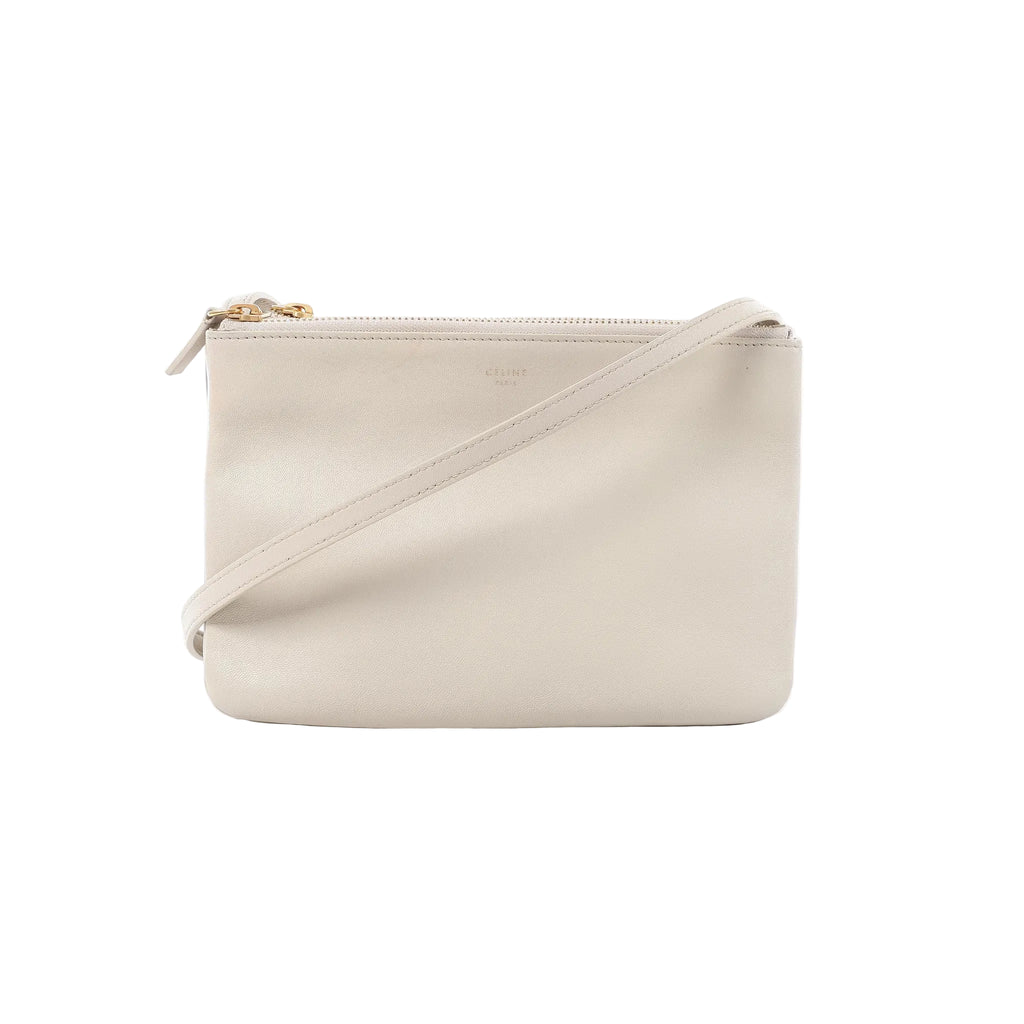 Celine Trio small crossbody bag in ecru leather with a minimalist rectangular shape, zip-top closure, gold-tone hardware, and slim shoulder strap on a white background.