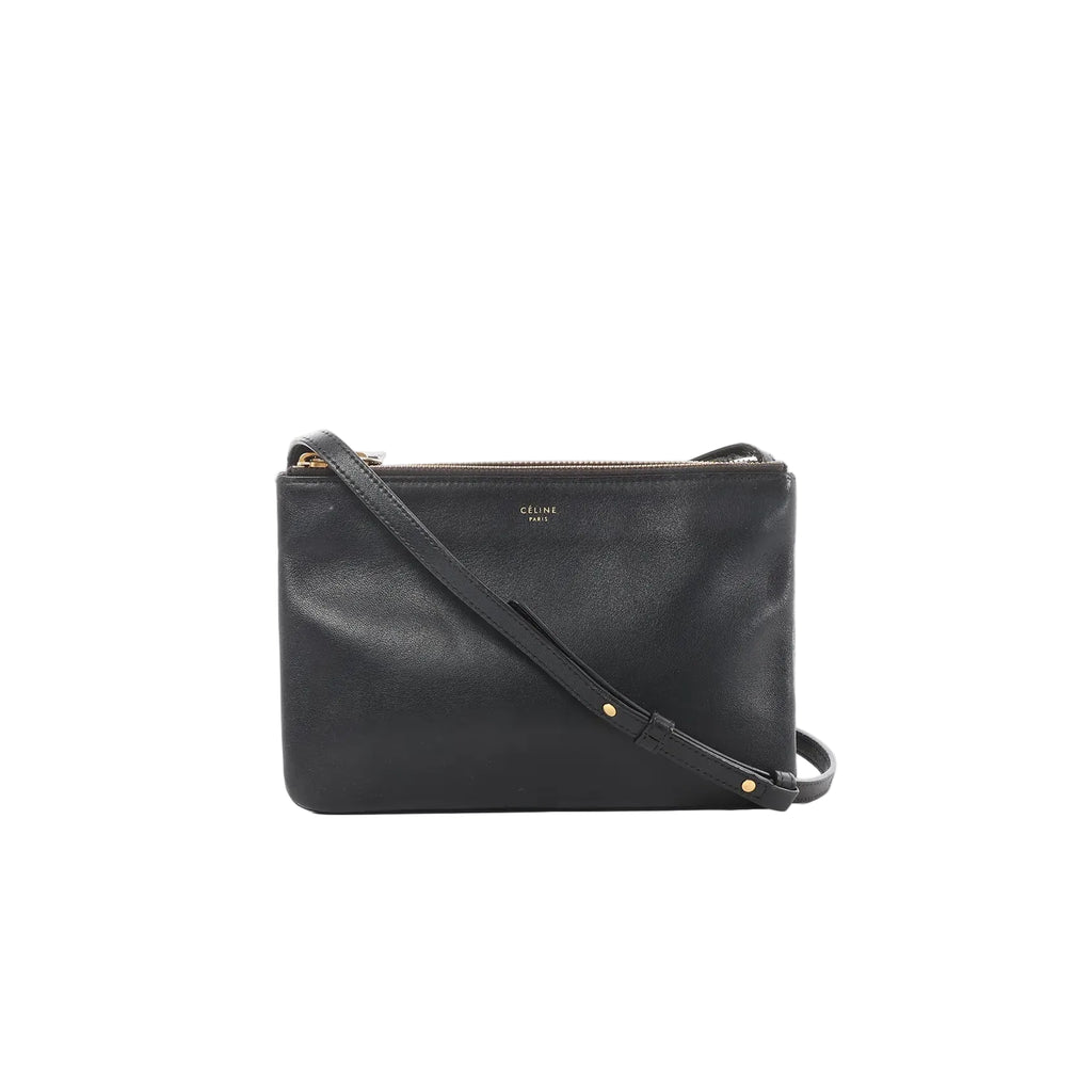 Black Celine Trio Small leather crossbody bag with zip-top closure, small gold logo, and slim strap with gold rivet details on a white background