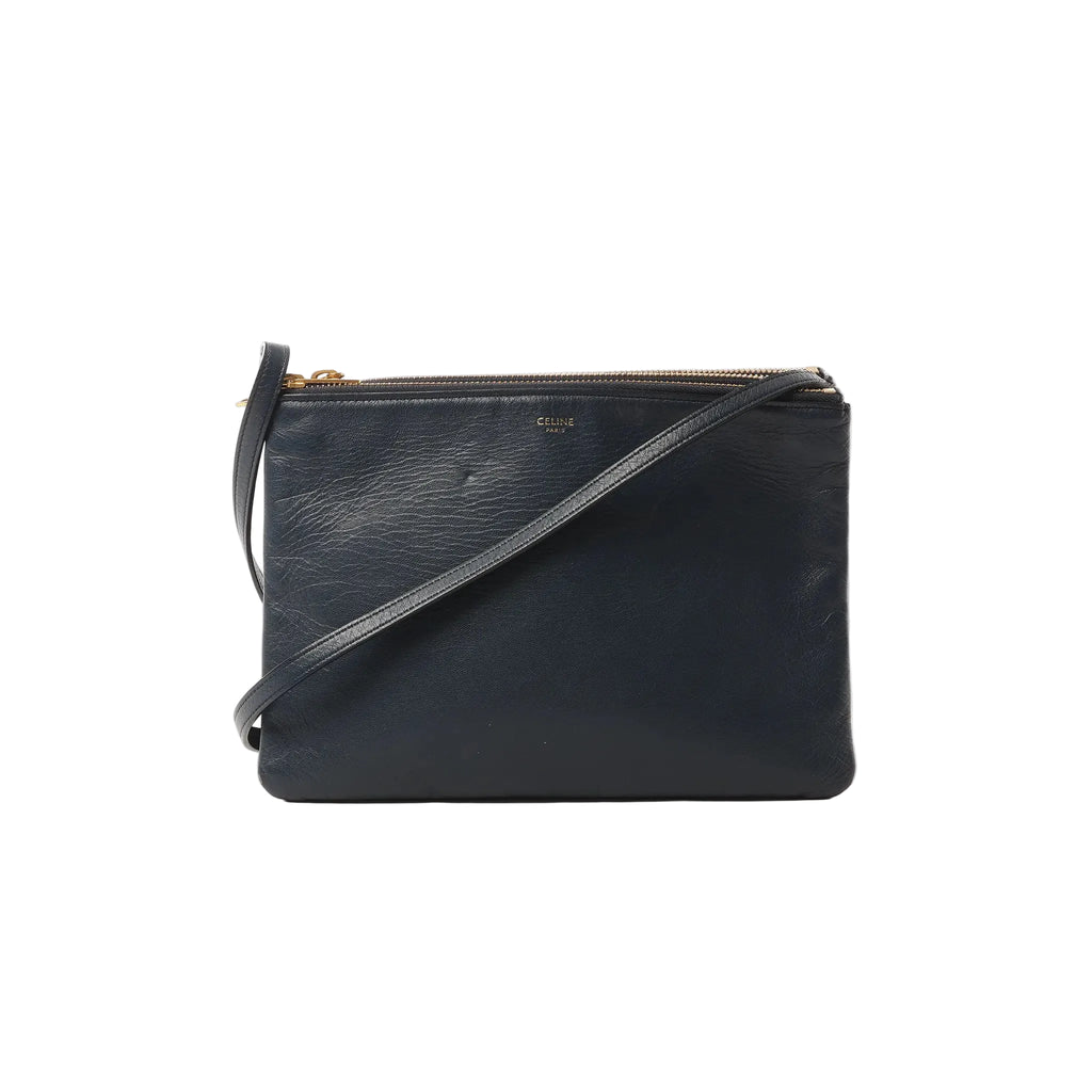 Black Celine Trio Large leather crossbody bag with gold-tone top zipper, slim strap, and small gold Celine Paris logo on front, on white background.