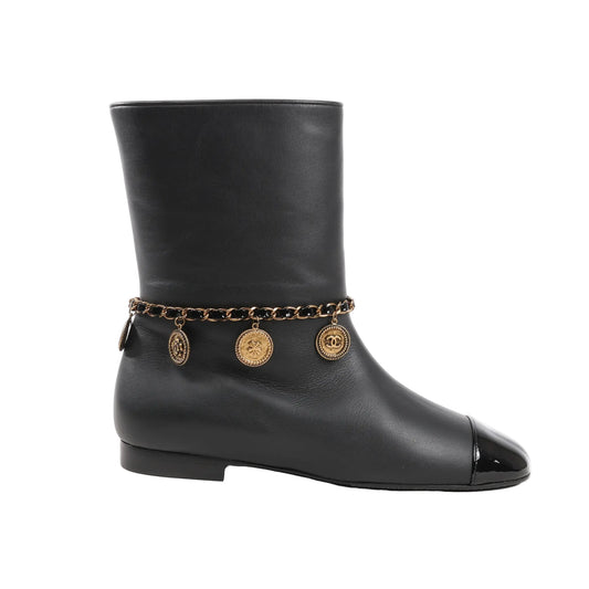 Chanel Coco Mark Camelia 17A ankle boots in smooth black leather featuring a black patent cap toe, gold-tone chain with hanging logo and clover charms, and a low-profile heel. Size 36 EU.