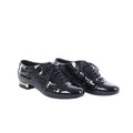 Black Chanel patent leather lace-up shoes displayed beside a black Chanel box, dust bags and white cards.