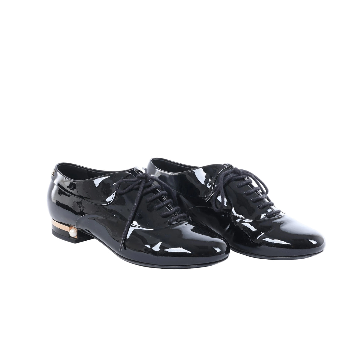 Black Chanel patent leather lace-up shoes displayed beside a black Chanel box, dust bags and white cards.