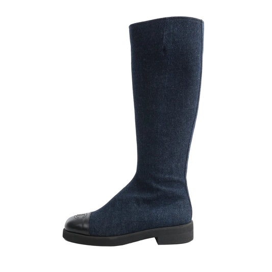 Side view of a navy blue Chanel Coco Mark long boot in size 37 EU, crafted from denim with a black leather cap toe featuring the embossed Chanel logo, and finished with a low black block heel on a white background.