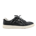 Side view of a black Chanel leather low-top sneaker with Chanel-lettered black laces, white collar trim and an off-white sole.