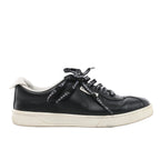 Side view of a black Chanel leather low-top sneaker with Chanel-lettered black laces, white collar trim and an off-white sole.