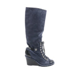 Chanel long boot in navy suede with black patent toe and wedge heel, lace-up front with silver eyelets, and black Chanel logo ankle detail, side view on white background