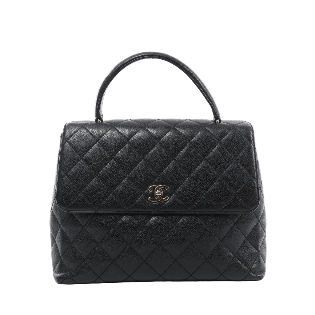Front view of a black Chanel Kelly handbag with grained leather, diamond quilting, a curved top handle and a silver-tone CC turn-lock on the flap.