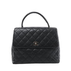 Front view of a black Chanel Kelly handbag with grained leather, diamond quilting, a curved top handle and a silver-tone CC turn-lock on the flap.