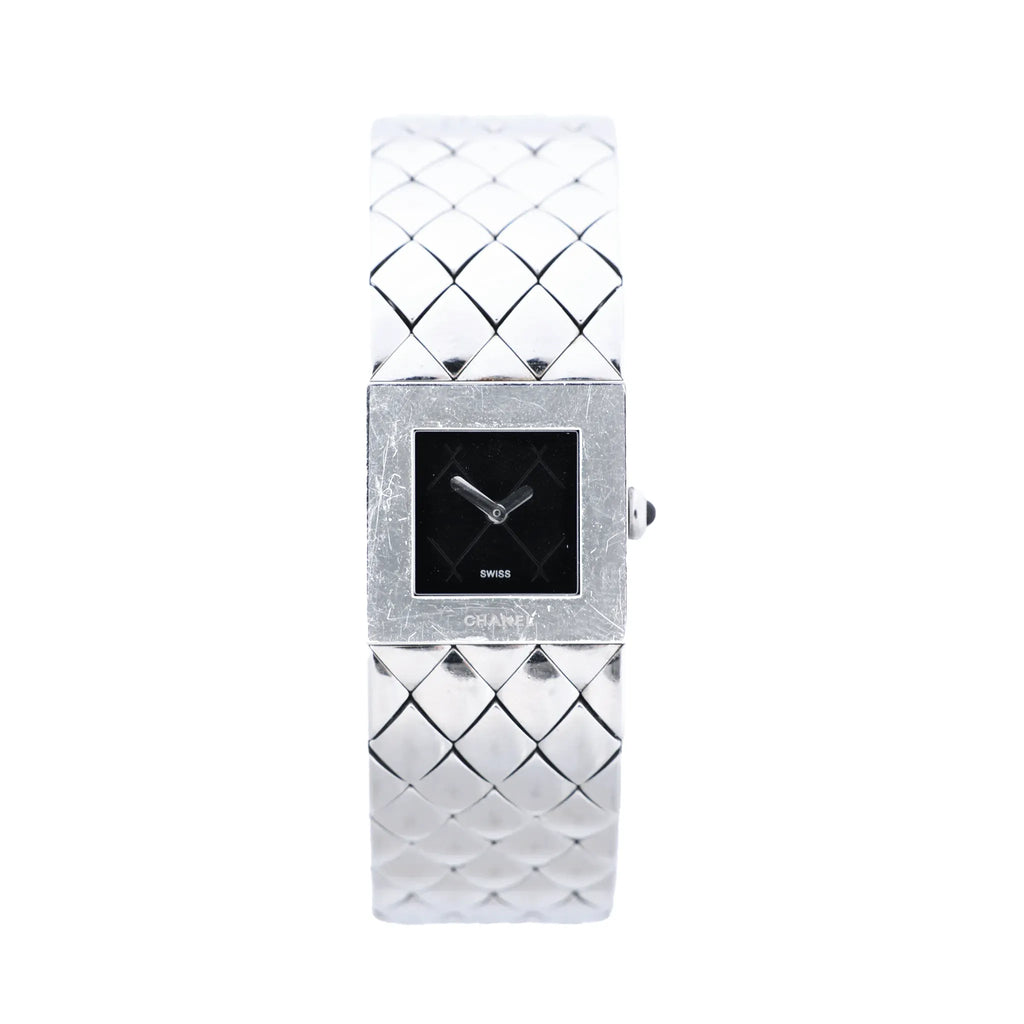 Chanel Matelassé stainless steel watch with black square dial, polished square case, quilted bracelet pattern, silver-tone hands and side crown on white background.